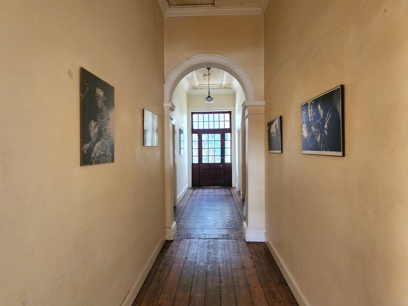 A long hallway featuring original timber floorboards, a classic architectural archway, and a traditional timber front door with glass panels.