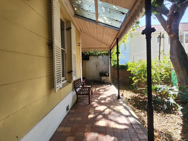 Covered veranda featuring tiled flooring, timber ceiling, and wrought iron columns, offering a shaded outdoor space with potential for cosmetic restoration.