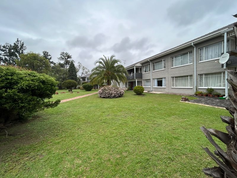 A view of the rear exterior of the flat complex, featuring a well-maintained communal lawn, landscaped garden, and paved pathways.