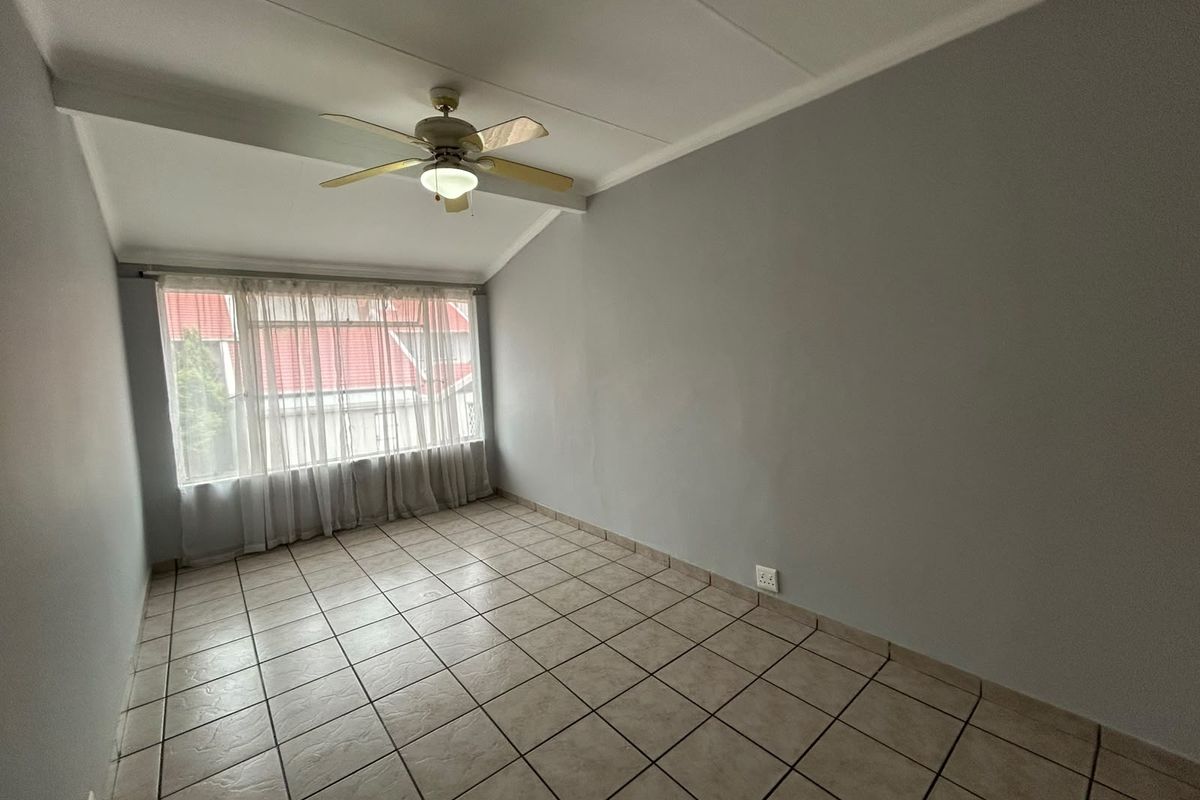 An empty bedroom featuring tiled flooring, a ceiling fan, and neutral grey walls, offering a blank canvas for personalization.