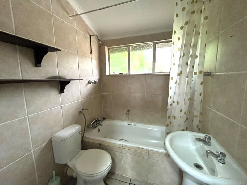 A functional bathroom featuring a bathtub with shower attachment, pedestal basin, toilet, and neutral wall tiling throughout.
