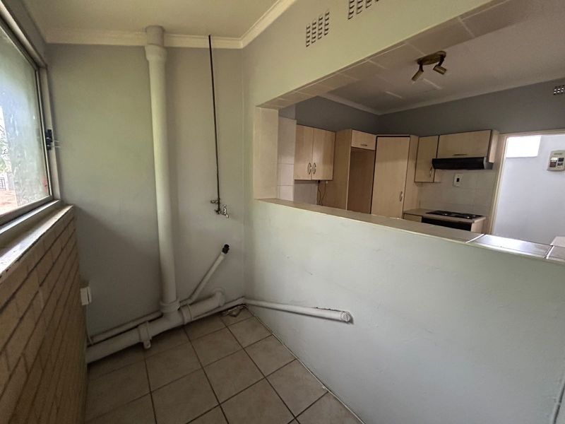 A functional scullery area featuring tiled flooring and exposed plumbing, with a convenient pass-through window connecting to the adjacent kitchen space.