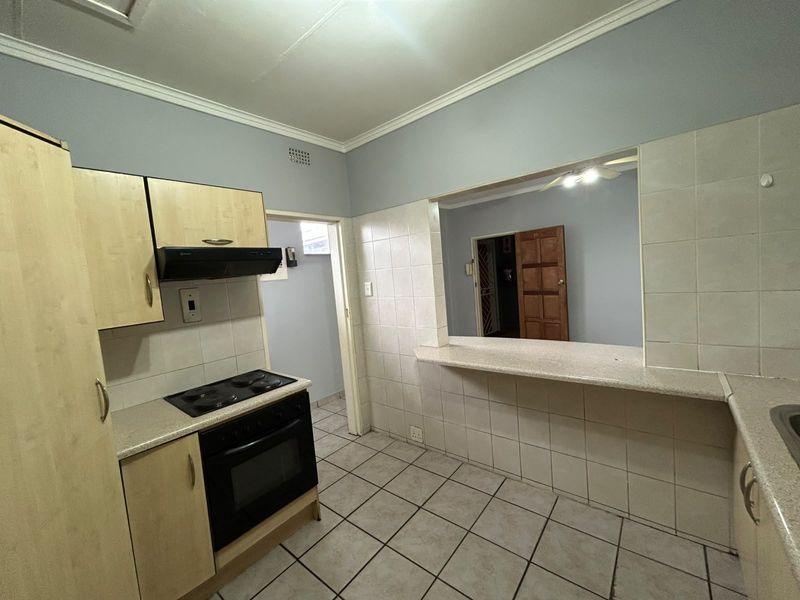 A functional kitchen featuring built-in cabinetry, electric oven and hob, tiled splashbacks, and a convenient breakfast bar opening into the adjacent living area.