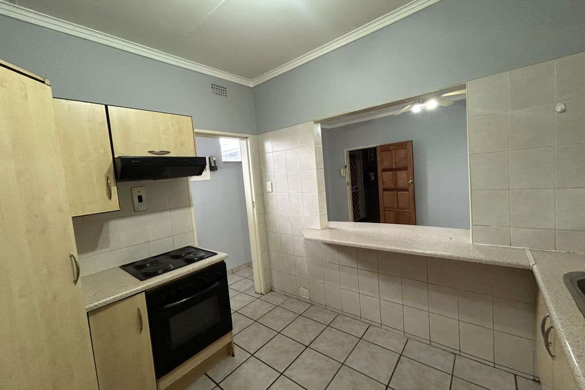 A functional kitchen featuring built-in cabinetry, electric oven and hob, tiled splashbacks, and a convenient breakfast bar opening into the adjacent living area.