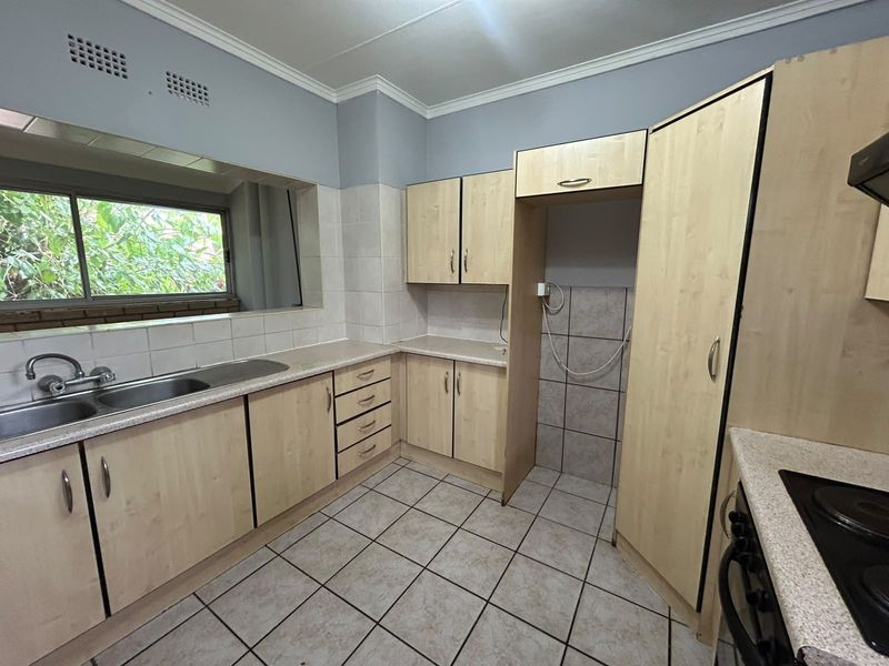 A functional kitchen featuring light wood-finish cabinetry, laminate countertops, a stainless steel double sink, and tiled flooring with a built-in hob and oven.