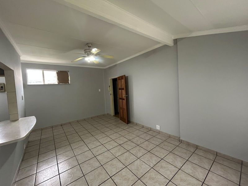 An empty open-plan living area featuring tiled flooring, a ceiling fan, and a breakfast bar, providing a neutral canvas for interior design.