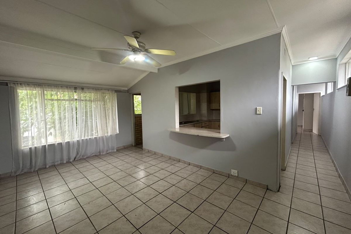 Spacious living area featuring tiled flooring, a ceiling fan, and a convenient serving hatch connecting to the kitchen.