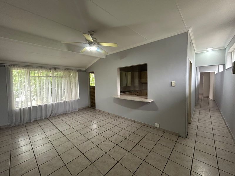 Spacious living area featuring tiled flooring, a ceiling fan, and a convenient serving hatch connecting to the kitchen.