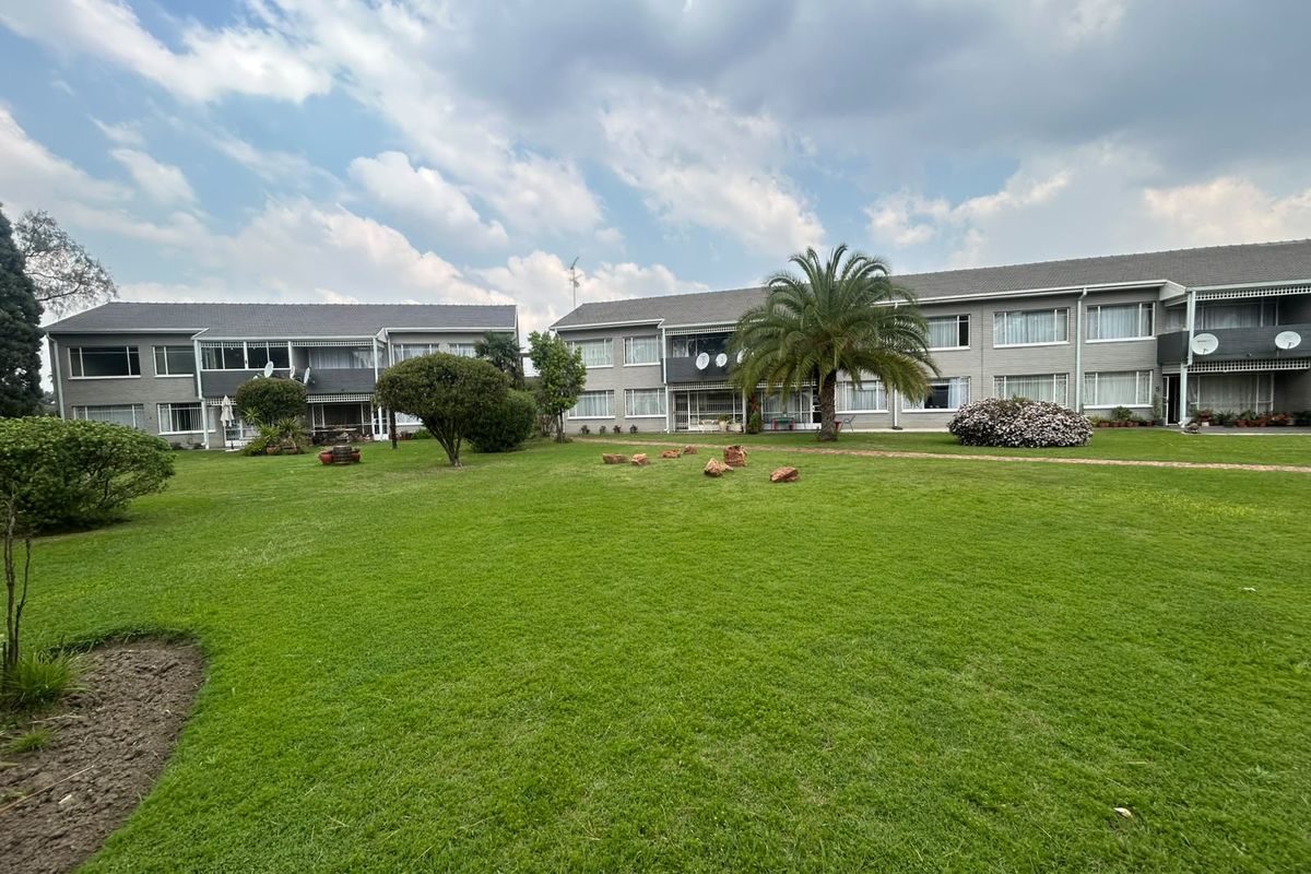 A view of the rear elevation of the apartment complex, featuring well-maintained communal lawns, landscaped gardens, and multi-story residential units with balconies.