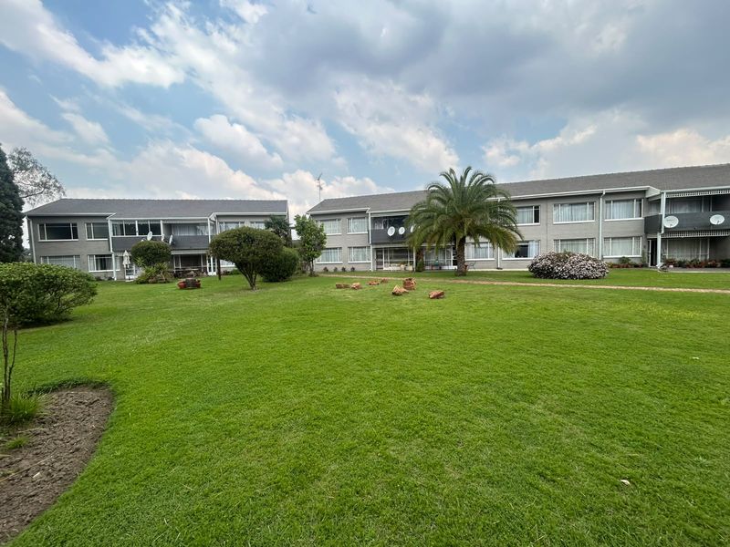 A view of the rear elevation of the apartment complex, featuring well-maintained communal lawns, landscaped gardens, and multi-story residential units with balconies.