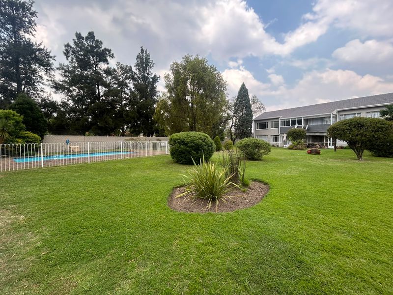 A well-maintained communal garden area featuring a fenced swimming pool and expansive lawn space within the flat complex grounds.