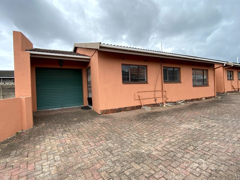 Front elevation of a townhouse featuring a single garage, paved driveway, and security-fitted windows with a terracotta-toned exterior finish.