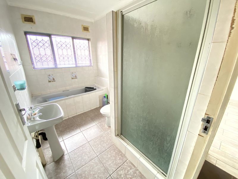 A dated bathroom featuring a pedestal basin, built-in bathtub, and separate shower enclosure with tiled finishes throughout.