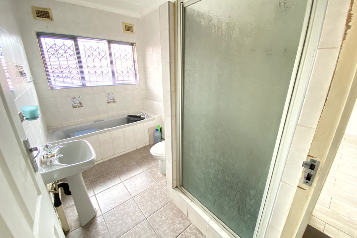 A dated bathroom featuring a pedestal basin, built-in bathtub, and separate shower enclosure with tiled finishes throughout.