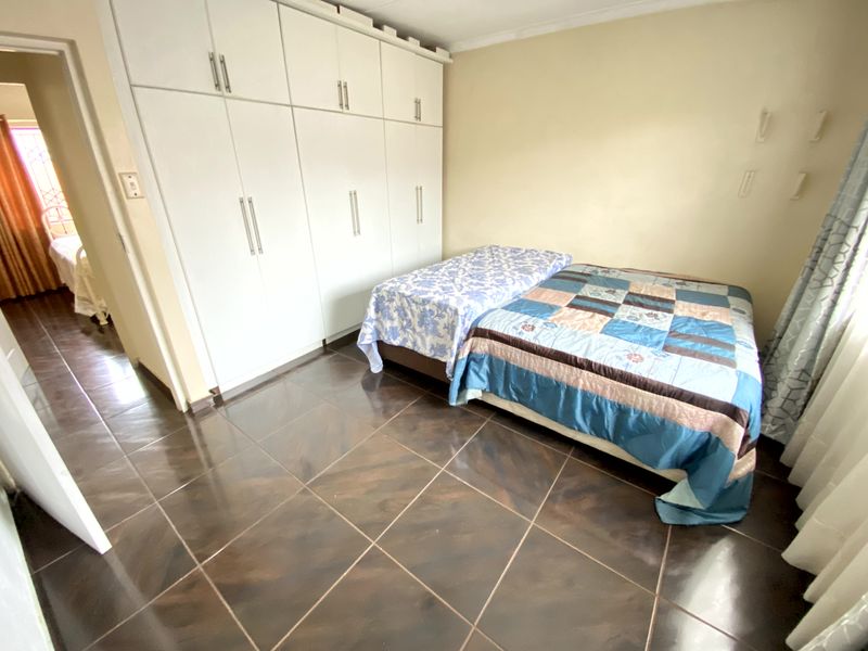 A bedroom featuring built-in cupboards and dark tiled flooring, with a view into an adjacent room.