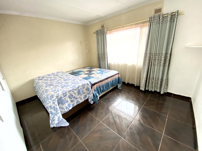 A standard bedroom featuring dark tiled flooring, neutral wall finishes, and large windows with installed curtain rails.