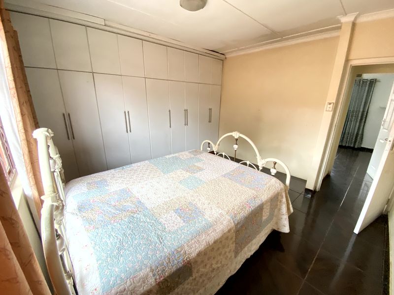 A bedroom featuring built-in cupboards and dark tiled flooring, requiring some cosmetic updates to the ceiling and walls.
