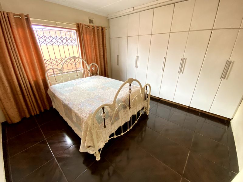 A bedroom featuring dark tiled flooring, extensive built-in cupboards for storage, and a window fitted with security bars.