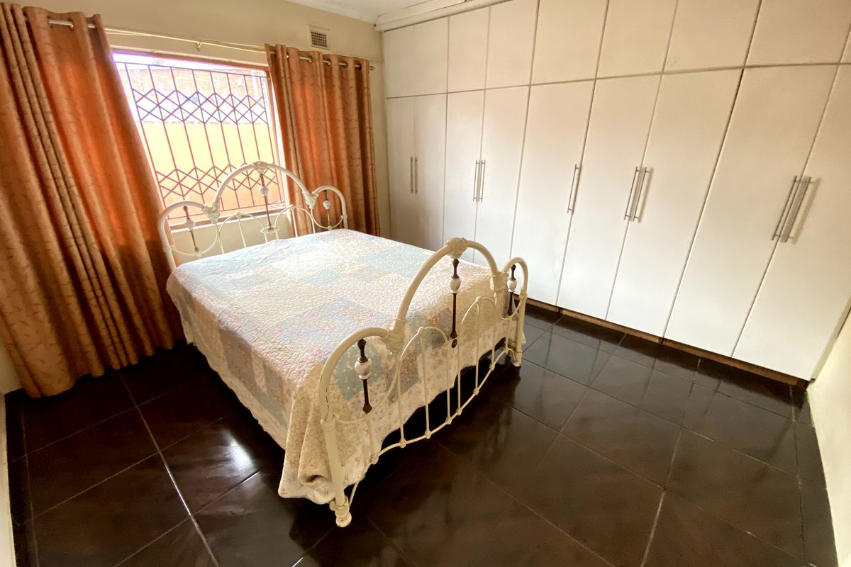 A bedroom featuring dark tiled flooring, extensive built-in cupboards for storage, and a window fitted with security bars.