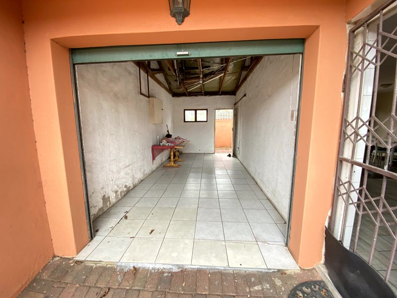A single garage space featuring tiled flooring and an exposed roof structure, requiring maintenance and repair to the walls and ceiling.