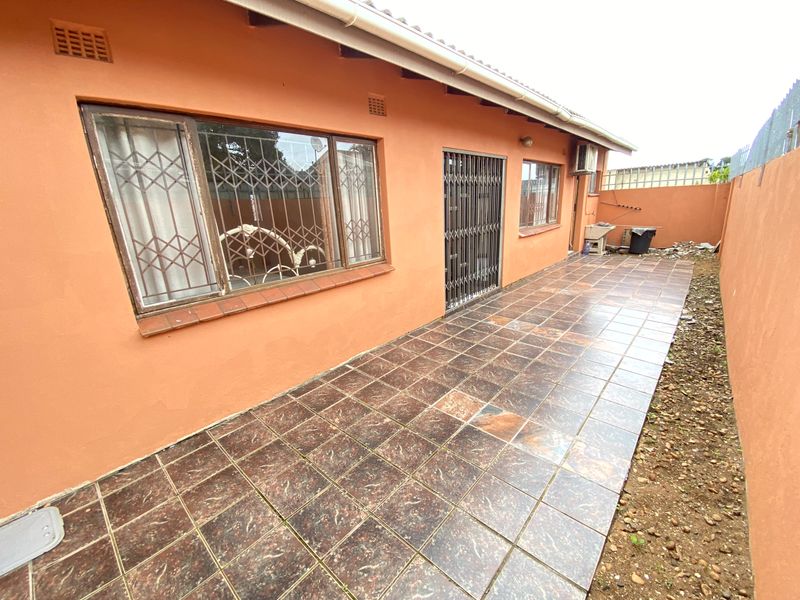 Rear exterior view of the townhouse featuring a tiled patio area, security gates, and an external wash basin along the side wall.