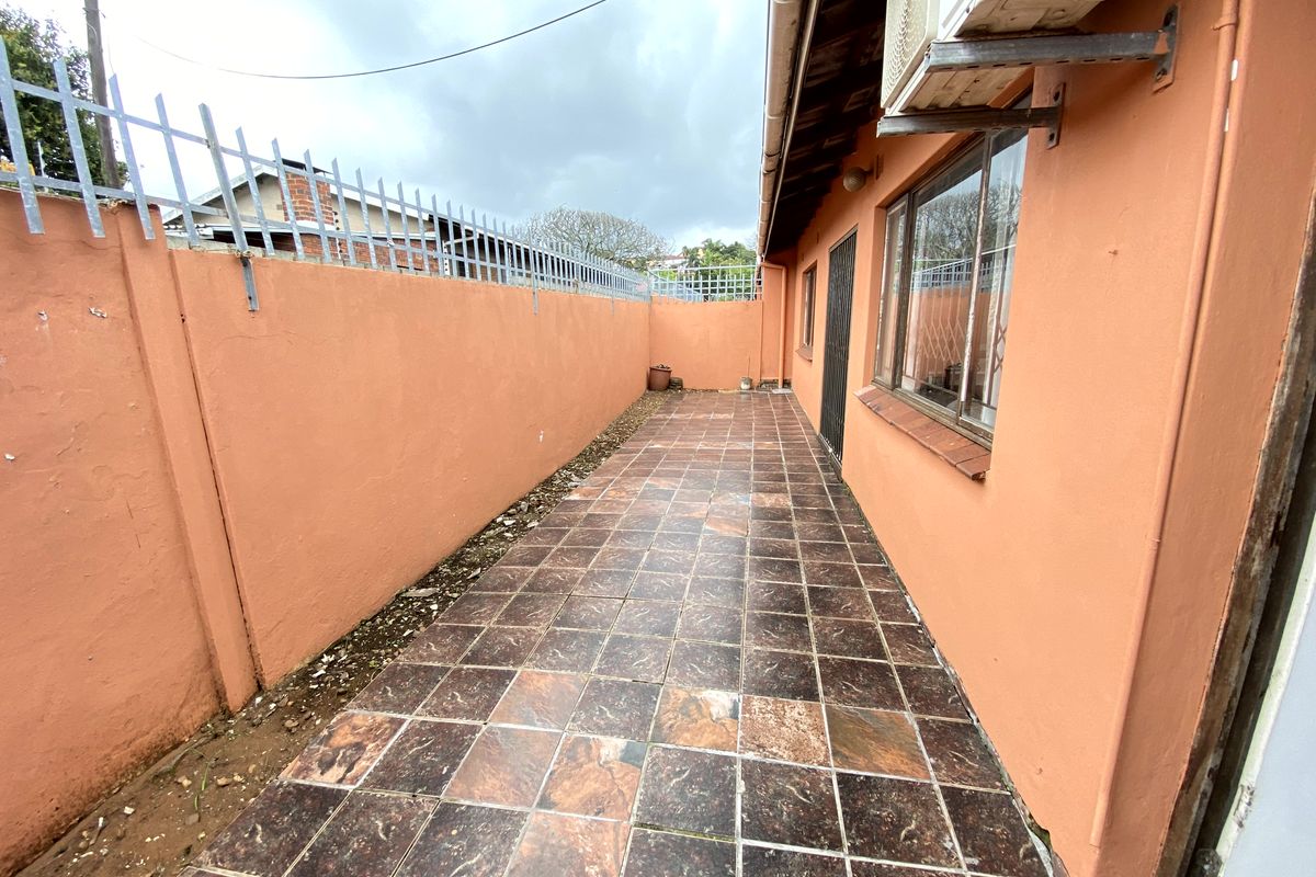 A narrow rear exterior patio area featuring tiled flooring, perimeter wall with security spikes, and an external air conditioning unit.