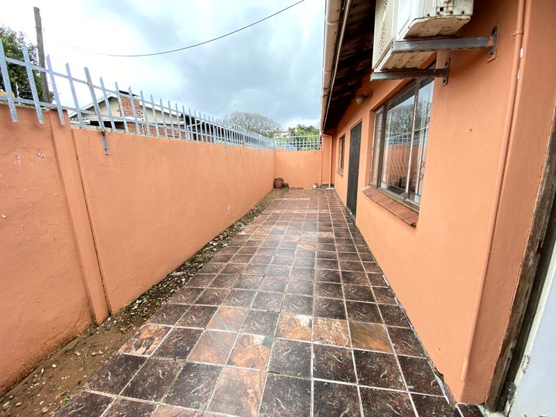 A narrow rear exterior patio area featuring tiled flooring, perimeter wall with security spikes, and an external air conditioning unit.