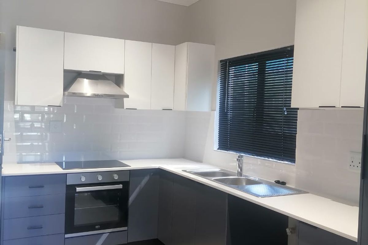Modern kitchen featuring two-tone cabinetry, integrated oven and hob, tiled splashback, and a double sink with contemporary finishes.