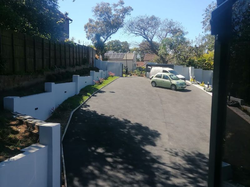 A view of the property's paved driveway and entrance area, featuring modern retaining walls and perimeter fencing.