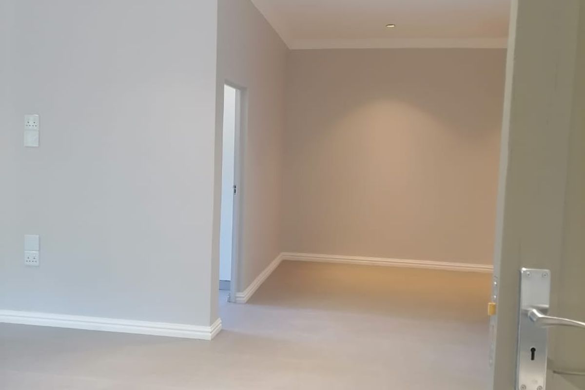 A bright, empty living area featuring neutral tiled flooring, recessed downlighting, and clean finishes, offering a versatile blank canvas for interior design.