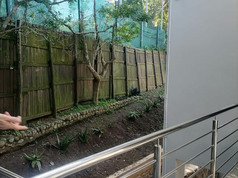A balcony area featuring a modern stainless steel balustrade overlooking a landscaped garden with a timber boundary fence.