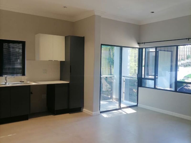 A bright, modern open-plan living and kitchen area featuring neutral tiled floors, sleek built-in cabinetry, and large sliding doors leading to an outdoor space.