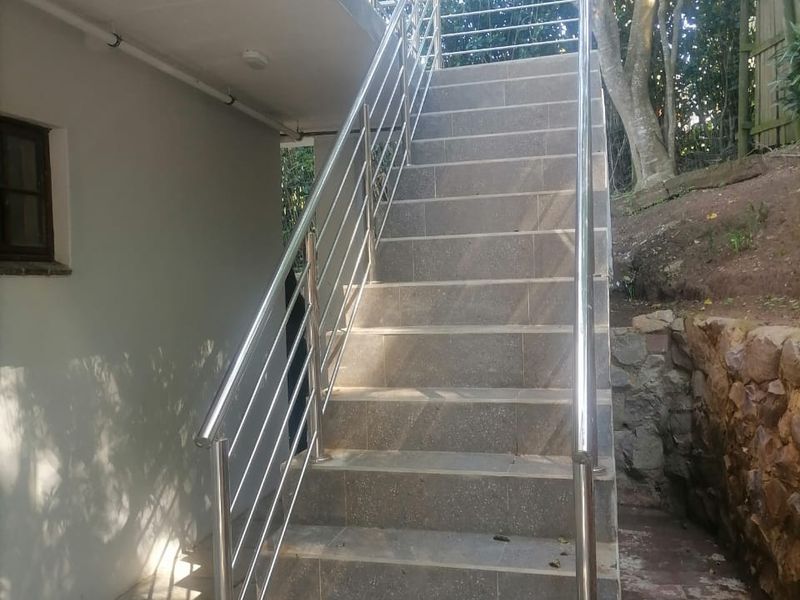 Exterior staircase featuring modern stainless steel balustrades and tiled steps, leading to an upper level with a natural stone retaining wall.
