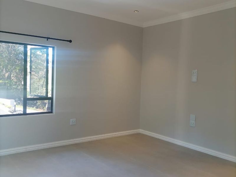 A bright, empty bedroom featuring neutral wall paint, tiled flooring, recessed downlights, and large aluminium-framed windows.