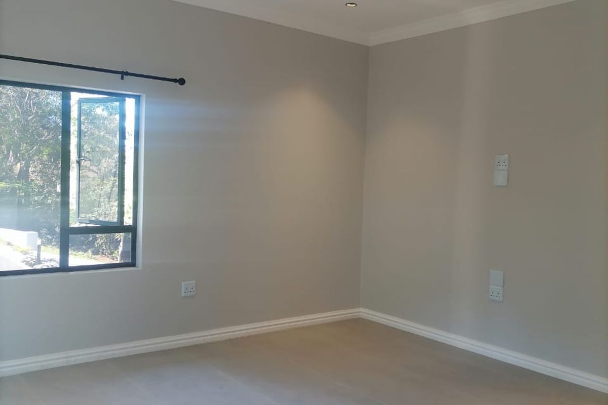 A bright, empty bedroom featuring neutral wall paint, tiled flooring, recessed downlights, and large aluminium-framed windows.