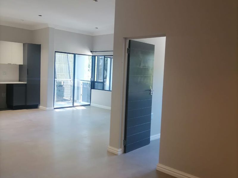 Spacious open-plan living area featuring modern neutral finishes, recessed lighting, and direct access to a balcony through sliding glass doors.
