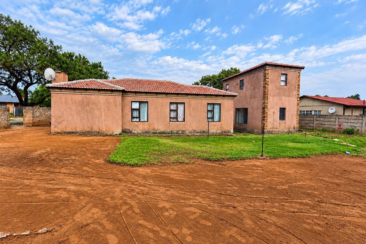 Rear view of a two-story house featuring terracotta roof tiles, stucco walls with stone accents, and aluminium window frames set on a large plot.
