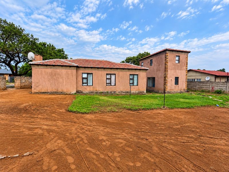 Rear view of a two-story house featuring terracotta roof tiles, stucco walls with stone accents, and aluminium window frames set on a large plot.