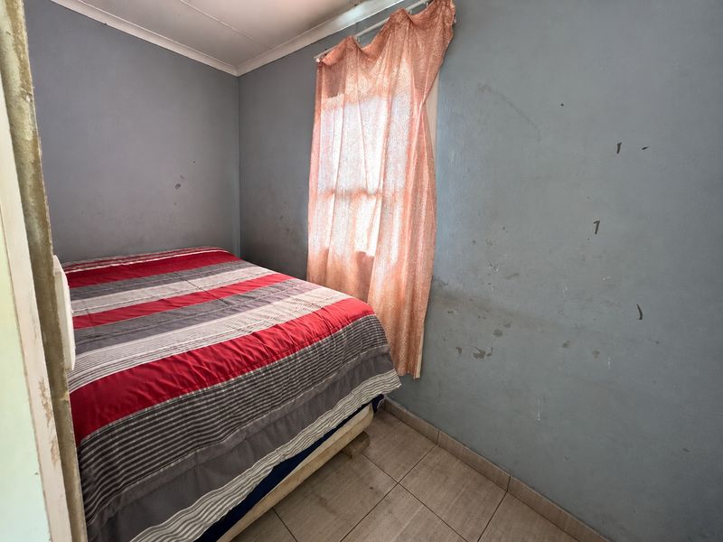 A compact bedroom featuring tiled flooring and coved ceilings, currently requiring cosmetic updates to the wall finishes.