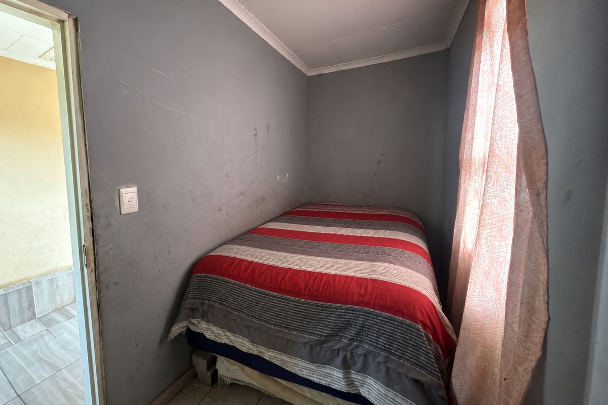 A compact bedroom featuring tiled flooring and coved ceilings, currently requiring cosmetic updates to the wall finishes.