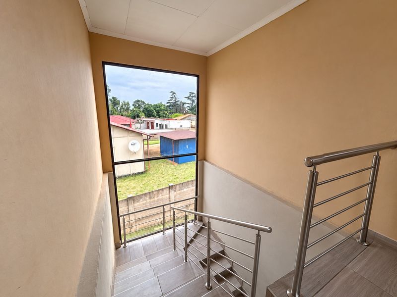 A bright staircase landing featuring modern stainless steel balustrades, tiled flooring, and a large window providing natural light and views of the exterior.