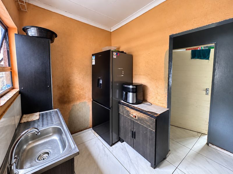 A small kitchen area featuring a stainless steel sink, tiled flooring, and significant wall surface wear requiring maintenance and cosmetic updates.