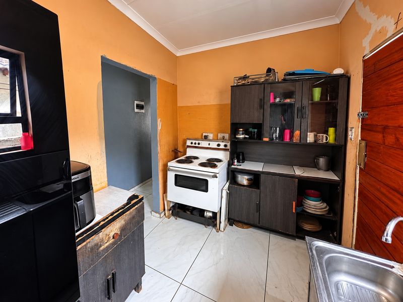 A dated kitchen featuring tiled floors, a freestanding electric stove, and basic cabinetry, requiring cosmetic updates and wall finishing to improve its overall appeal.