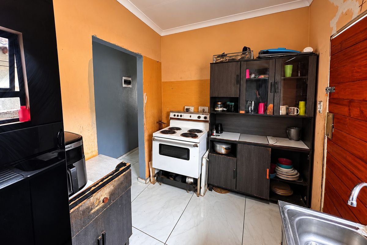 A dated kitchen featuring tiled floors, a freestanding electric stove, and basic cabinetry, requiring cosmetic updates and wall finishing to improve its overall appeal.