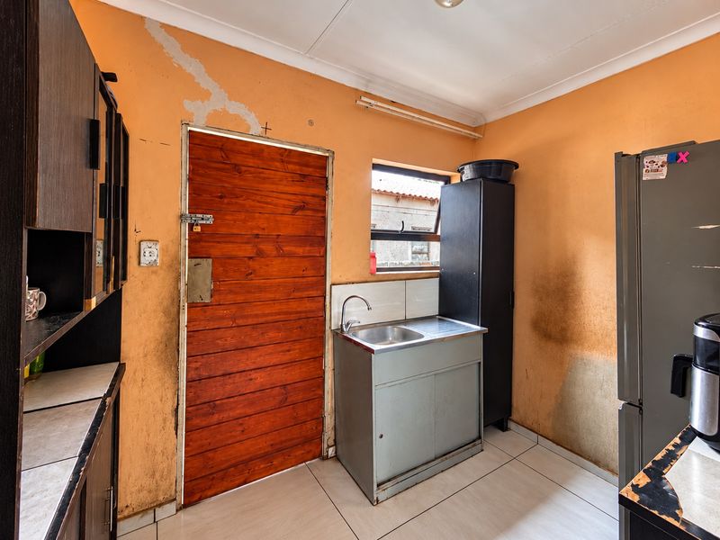 A functional scullery area featuring a stainless steel sink, tiled flooring, and built-in cabinetry, currently requiring cosmetic updates and wall repairs.
