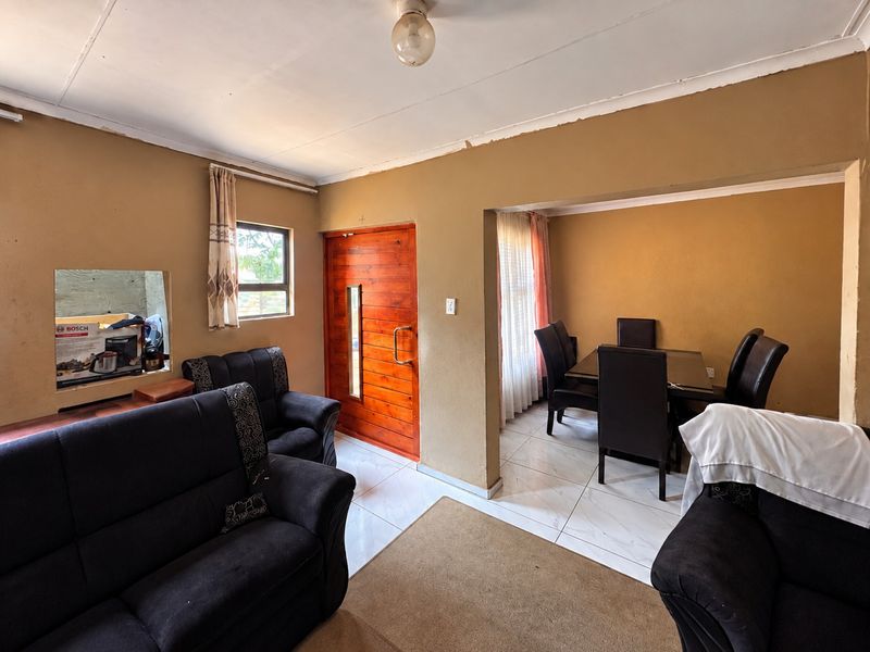 Open plan living and dining area featuring tiled flooring, a wooden front door, and a convenient serving hatch connecting to the kitchen area.