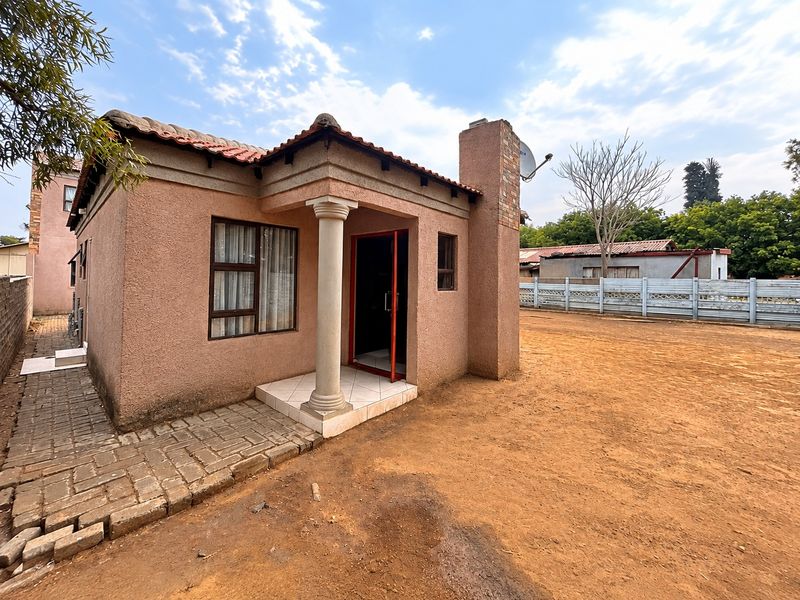Front view of a single-story house featuring a stucco facade, tiled roof, and a small covered entrance with a decorative column.
