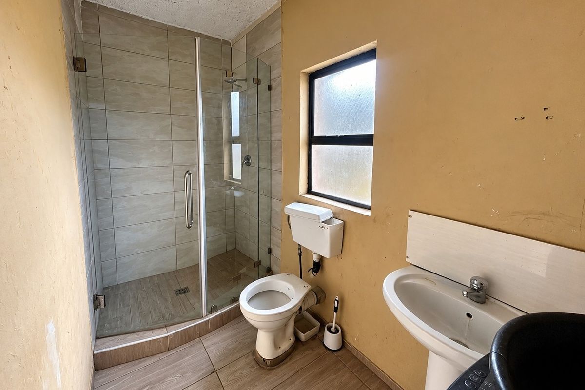 A functional bathroom featuring a glass-enclosed shower, pedestal basin, and toilet, with tiled finishes and potential for cosmetic updates to the wall surfaces.