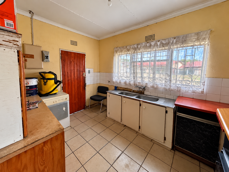 A dated kitchen featuring tiled flooring, a double bowl stainless steel sink, built-in cabinetry, and a timber door leading to the exterior.