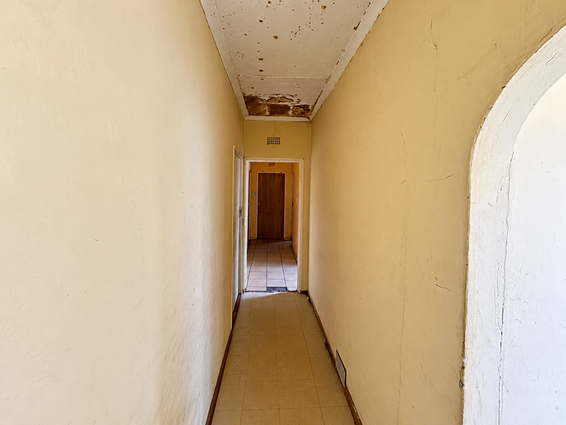 A narrow residential hallway featuring tiled flooring and an arched entryway, currently showing significant signs of wear and ceiling damage requiring maintenance.